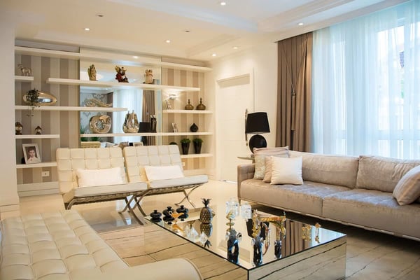 Luxury living room with cream sofa, modern chairs, glass coffee table, and built-in shelving displaying decorative objects