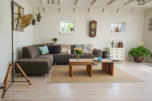 Bright living room with gray sectional sofa, wooden coffee table, white brick walls, and wooden beamed ceiling