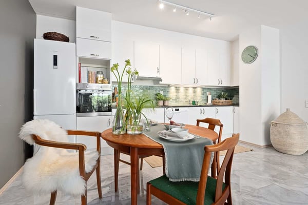 Modern kitchen with white cabinetry, green tile backsplash, and wooden dining table with place settings