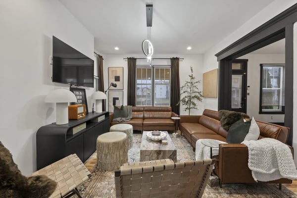 Modern living room with brown leather sectional, black media console, pendant light, and large windows with brown curtains