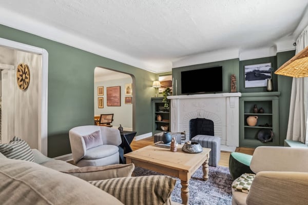 Living room with sage green walls, white fireplace, wooden coffee table, upholstered seating, and wall-mounted TV